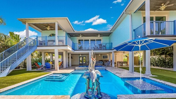 A two-story house with a large swimming pool, a statue, and a covered patio area.