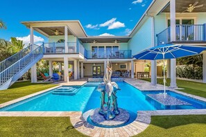 Une maison à deux étages avec une grande piscine, une statue et un patio couvert.