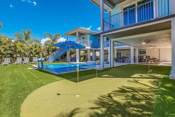 A pool area with a slide, umbrellas, and a putting green.