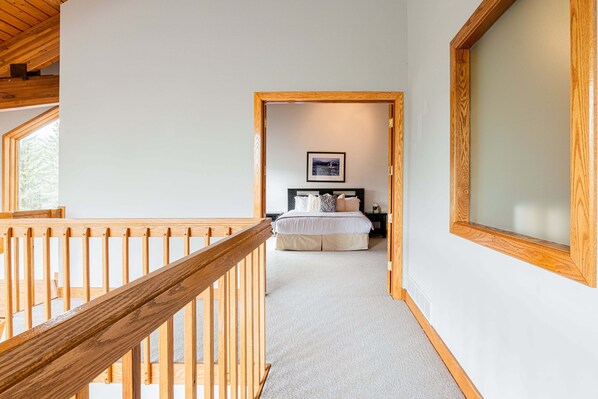 A bedroom with a bed, a nightstand, a framed picture on the wall, and a wooden railing.