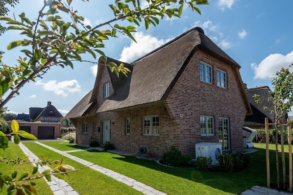 A two-story house with a brick exterior and a thatched roof.