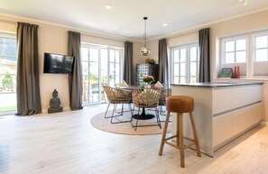 A modern kitchen with a dining area, large windows, and a TV.