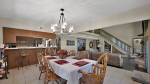 A spacious living area with a dining table set for four, a kitchen with modern appliances, and a staircase leading to an upper level. - Texas History Vacation House (Houston) (San Jacinto County)