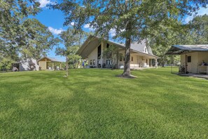 A large, single-story building with a sloped roof, surrounded by a well-maintained lawn and trees. - Ranch House and Moon House  (Houston) (San Jacinto County)