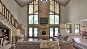 A spacious living room with a stone fireplace, a large sectional sofa, and a staircase leading to upper floors. - Texas History Vacation House (Houston) (San Jacinto County)