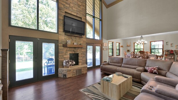 A spacious living room with a stone fireplace, large windows, a flat-screen TV, and a comfortable seating area. - Texas History Vacation House (Houston) (San Jacinto County)