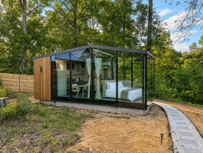 A modern glass-enclosed cabin with a bed and a dining area visible through the glass. - Ranch House and Moon House  (Houston) (San Jacinto County)