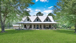 A large, single-story house with a symmetrical facade, a covered porch, and a well-maintained lawn. - Texas History Vacation House (Houston) (San Jacinto County)