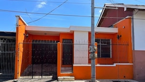 A two-story building with an orange facade, a gated entrance, and a visible utility pole. - Hostal Cisne House (León)