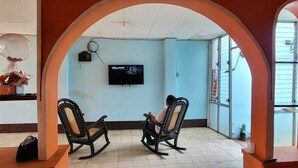 A room with two rocking chairs, a television mounted on the wall, and a window with metal bars. - Hostal Cisne House (León)