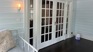 Una habitación con piso de madera oscura, paredes blancas con paneles y una puerta blanca con paneles de vidrio.
