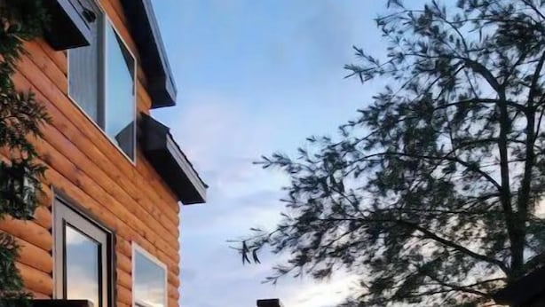A wooden cabin with a wooden deck and a view of a forested area.