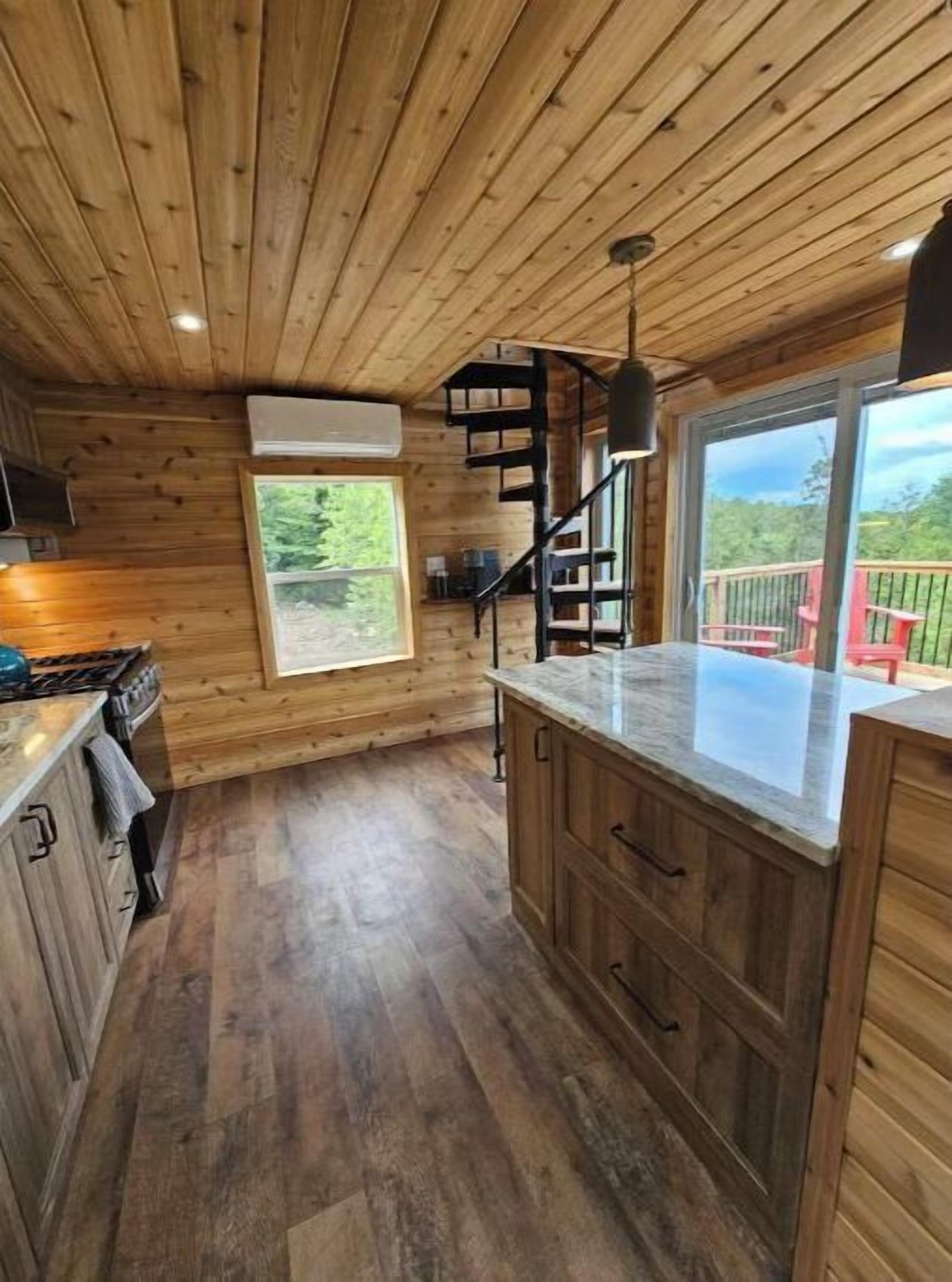 A wooden cabin kitchen with a central island, built-in cabinets, a stove, and a window overlooking a deck.