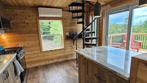 A wooden cabin kitchen with a central island, built-in cabinets, a stove, and a window overlooking a deck.