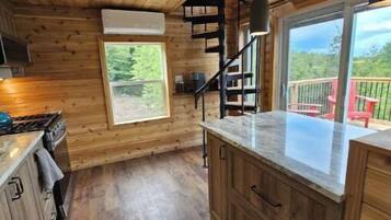 A wooden cabin kitchen with a central island, built-in cabinets, a stove, and a window overlooking a deck.