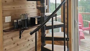 A spiral staircase in a wooden cabin with a small shelf holding a coffee maker and a container.