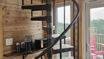 A spiral staircase in a wooden cabin with a small shelf holding a coffee maker and a container.
