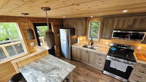 A modern kitchen with wooden cabinets, a stainless steel refrigerator, a microwave, and a marble countertop.