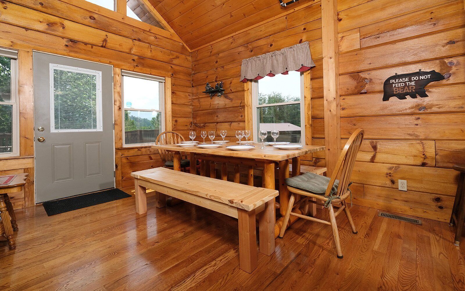 Interior de una cabaña de madera con una mesa de comedor para cuatro personas, un banco y una silla.