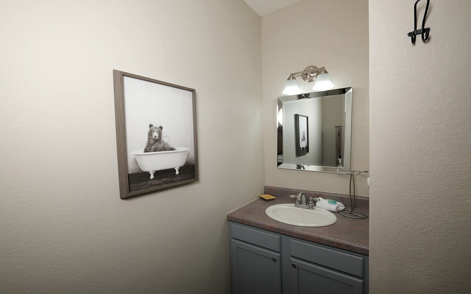 A bathroom with a white sink, a mirror, and a framed picture of a bear in a bathtub.