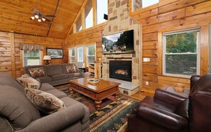 A cozy log cabin interior with a fireplace, wooden furniture, and large windows. - Mountain Views, Theater Room, Game Nights - 4 Cubs Cove (Pigeon Forge)