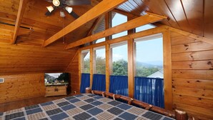 Quarto de cabana de madeira com uma cama grande, um ventilador de teto e uma TV sobre um aparador de madeira.