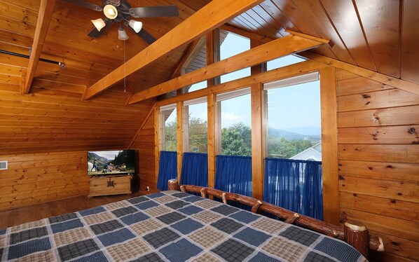 Relax in this cabin with a large bed, wooden dresser, and television, surrounded by a scenic view.