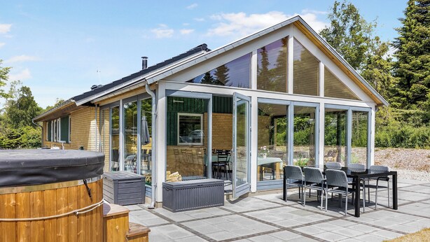 A modern house with a patio, a hot tub, and a glass-enclosed dining area.