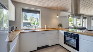 A modern kitchen with white cabinets, a wooden countertop, a built-in oven, and pendant lighting.