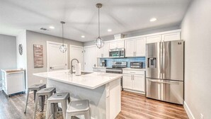 A modern kitchen with white cabinetry, stainless steel appliances, and a central island with stools.