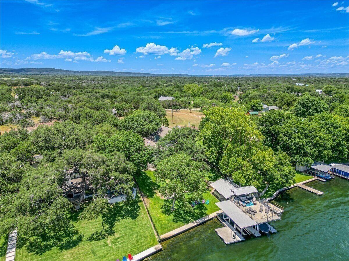 Vue aérienne d’une propriété au bord du lac, avec un quai, une maison dotée d’une terrasse et une végétation luxuriante tout autour.