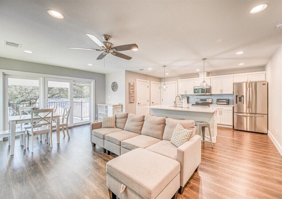A modern living room with a sectional sofa, dining area, and a kitchen with stainless steel appliances.