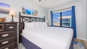 A hotel room with a bed, a dresser, a ceiling fan, and a large window with a view. - Island Winds West 871 2 Bedroom Condo (Gulf Shores)