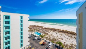 A beach view from a hotel balcony with a pool and parking area. - Island Winds West 871 2 Bedroom Condo (Gulf Shores)