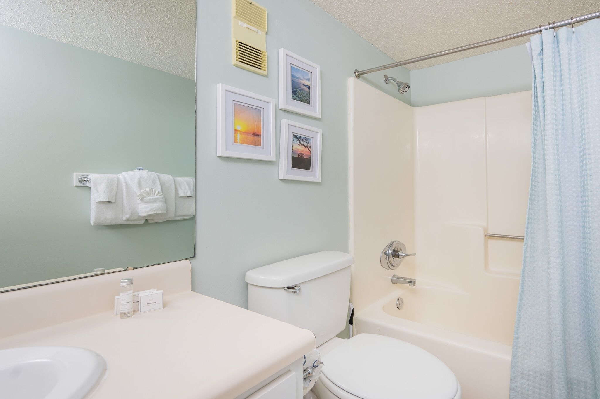 A bathroom with a toilet, sink, and bathtub. There are framed pictures on the wall, a towel rack with towels, and a shower curtain.