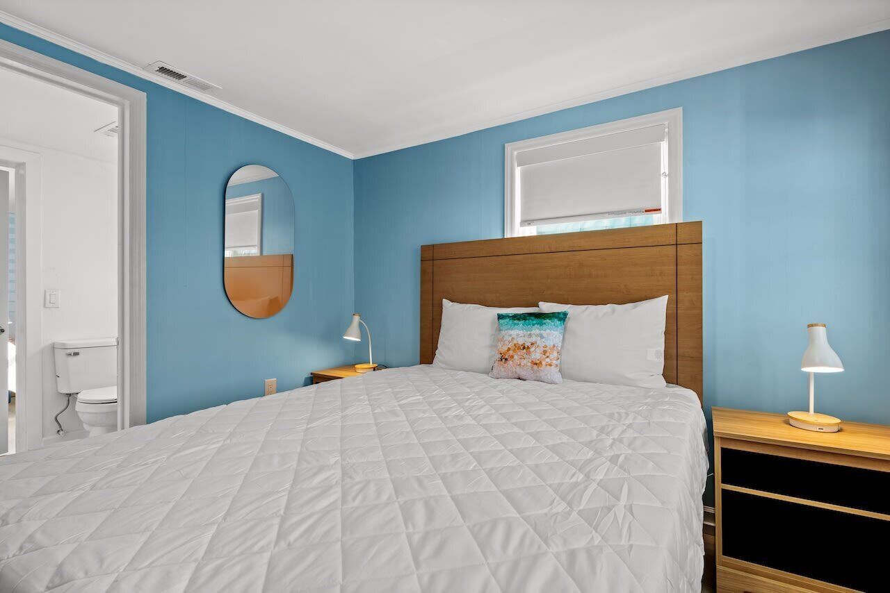 A bedroom with a large bed, a wooden headboard, a round mirror, and two bedside tables with lamps.