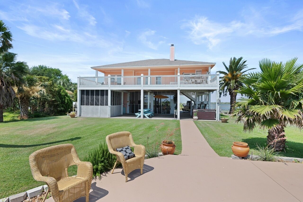 A two-story house with a balcony, a patio with wicker chairs, and a well-maintained lawn.