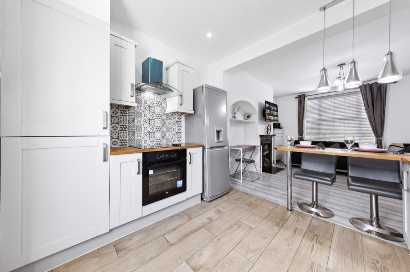 Una cocina moderna con armarios blancos, horno integrado, refrigerador y un área de comedor con taburetes de bar.