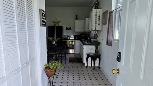 A narrow hallway with a patterned floor, leading to a kitchen area with white cabinets and a dining table. - Kingdom Home Country Cottage is where you can relax, rejuvenate and enjoy peace. (Waxahachie)