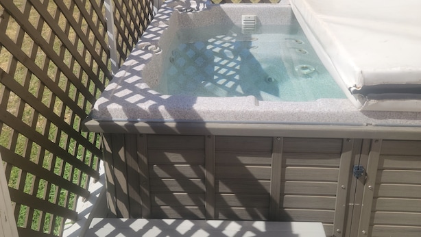 A hot tub with a wooden deck and a lattice fence, overlooking a field. - Kingdom Home Country Cottage is where you can relax, rejuvenate and enjoy peace. (Waxahachie)