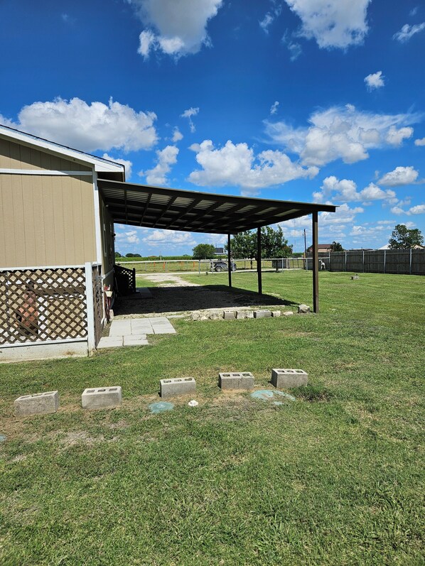 A covered patio area with a lawn, a building with a beige exterior, and a wooden fence in the background.