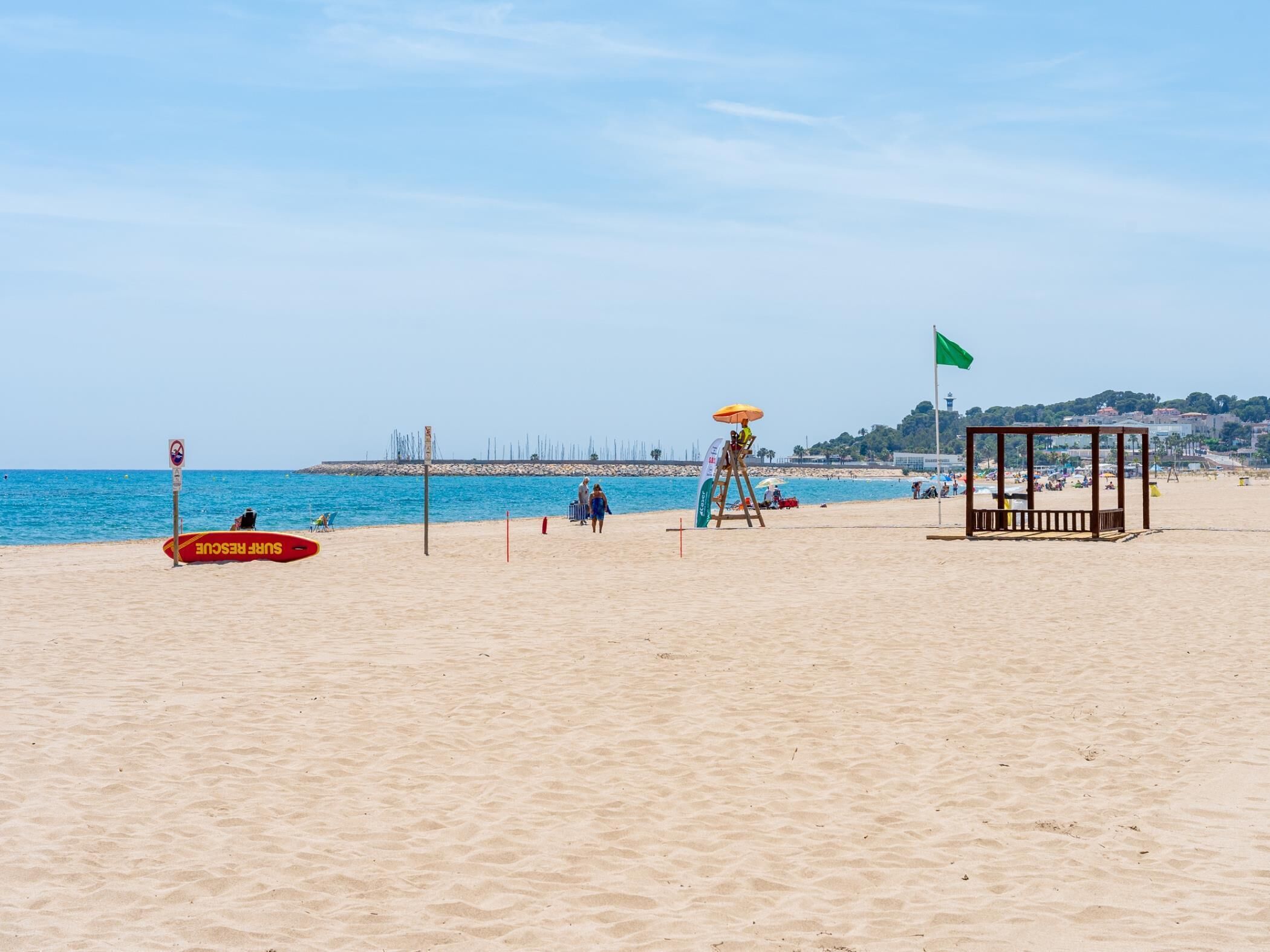 A beach with a lifeguard tower, a lifeguard stand, and a beach umbrella.