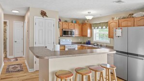 A kitchen with wooden cabinets, a stainless steel refrigerator, a microwave, and a stove. There are three wooden stools at the island. - Spacious Beach House, Private Pool, Short Walk to the Beach, Bikes Welcome (Murrells Inlet)