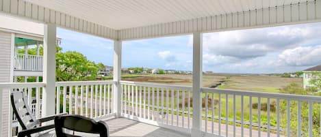 A covered porch with white railings and a view of a grassy landscape.