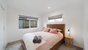 Ein Schlafzimmer mit einem hölzernen Kopfteil, einem Bett mit pinkener Bettwäsche, zwei gerollten Handtüchern, einer Nachttischlampe und einem kleinen runden Tisch.