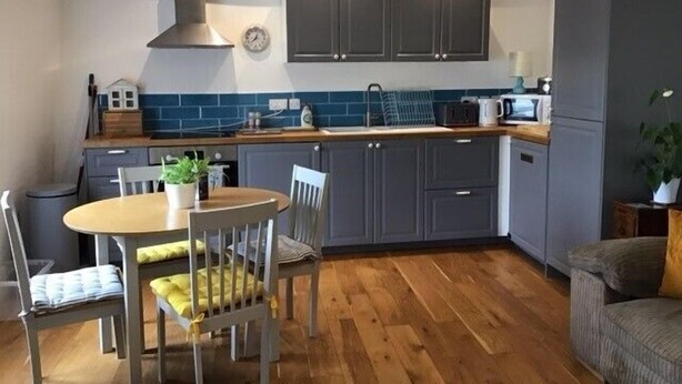 A compact kitchen with grey cabinets, a round wooden table, and a dining chair. - Central Teignmouth Penthouse, Sleeps 4, Pets Ok (Teignmouth)