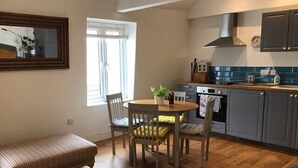 A compact kitchen with wooden flooring, a dining table with chairs, a bench, and a window with curtains. - Central Teignmouth Penthouse, Sleeps 4, Pets Ok (Teignmouth)