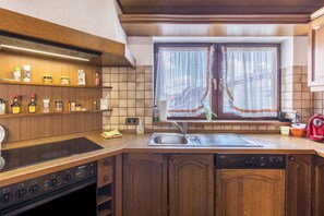 Eine Küche mit Holzschränken, einem Einbauherd, einem Spülbecken und einem Fenster mit Spitzenvorhängen.