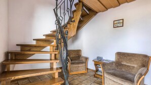 A wooden staircase with a metal railing leading to a loft area. There is a brown armchair and a small table with books.
