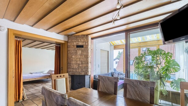 A room with a wooden ceiling, a dining table with chairs, a bed, a fireplace, and a TV.